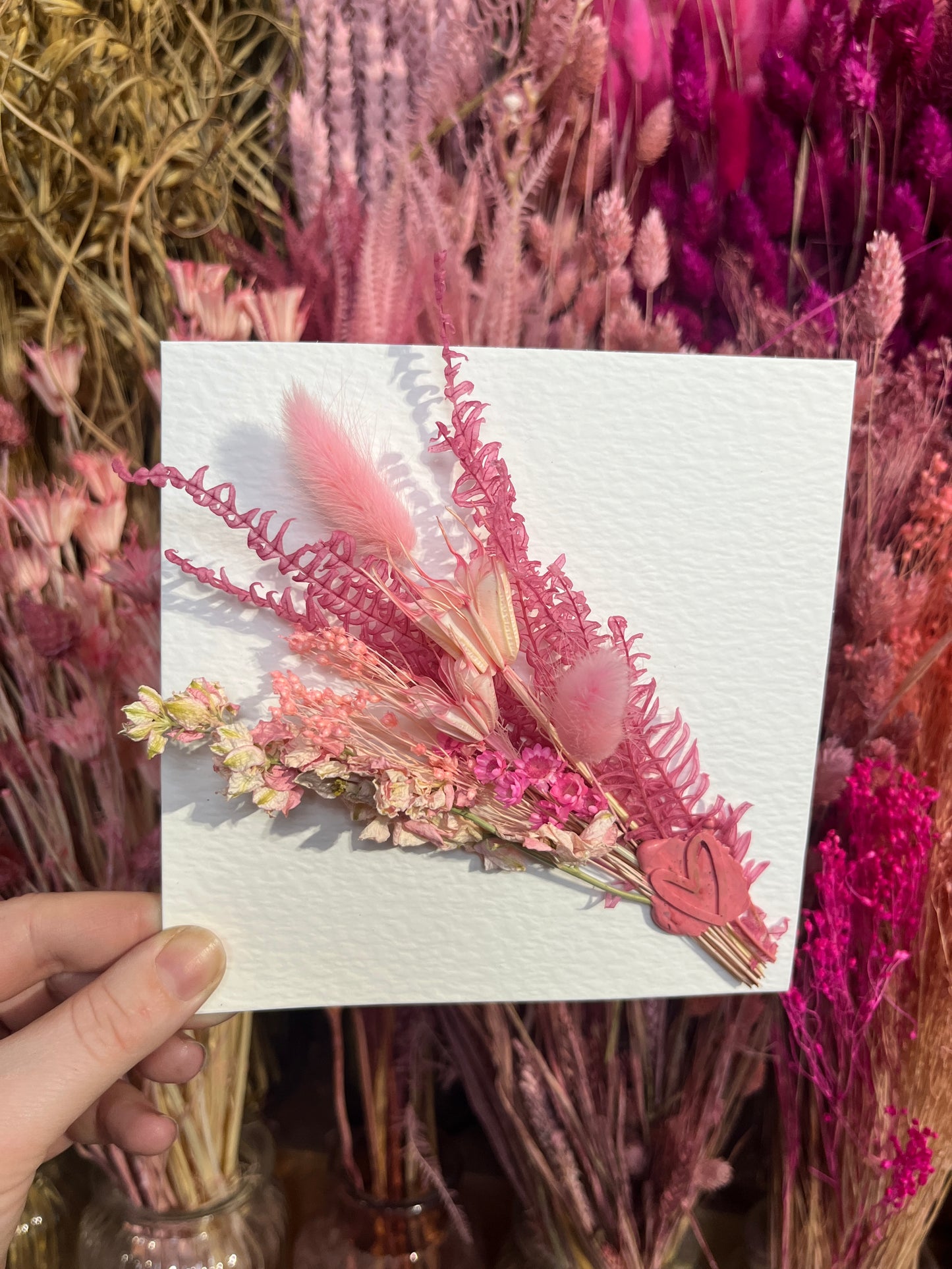 Kayleigh holding a pink dried flowers card with a background of flowers