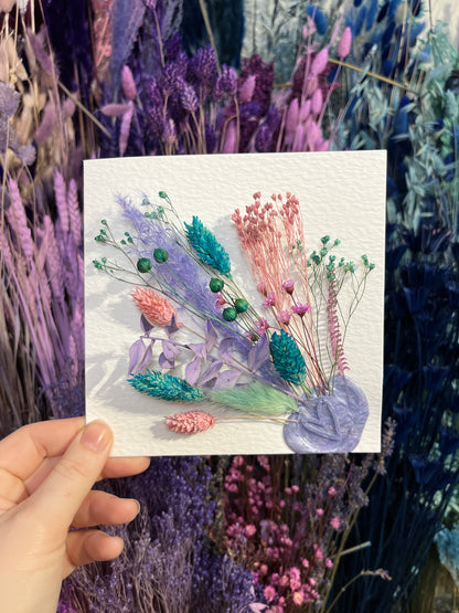 Kayleigh holding a multicoloured dried flowers card with a background of flowers