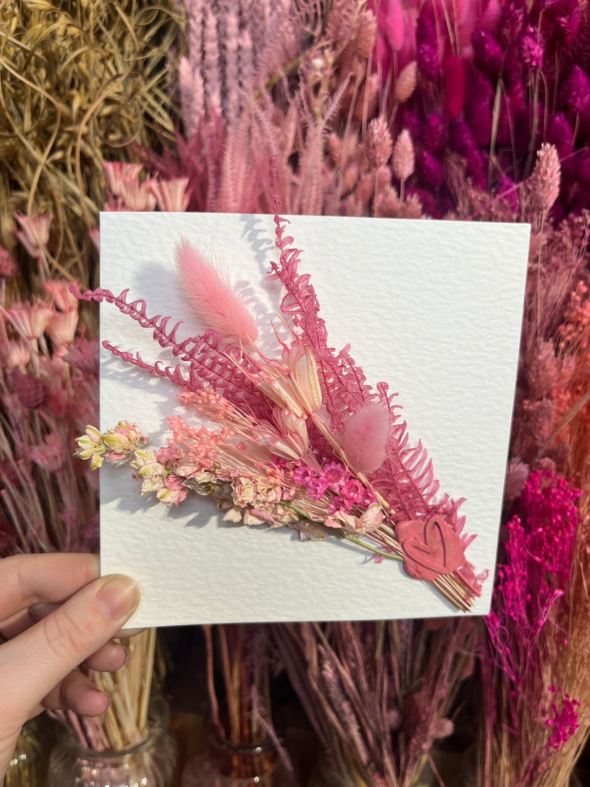  Kayleigh holding a pink dried flowers card with a background of flowers