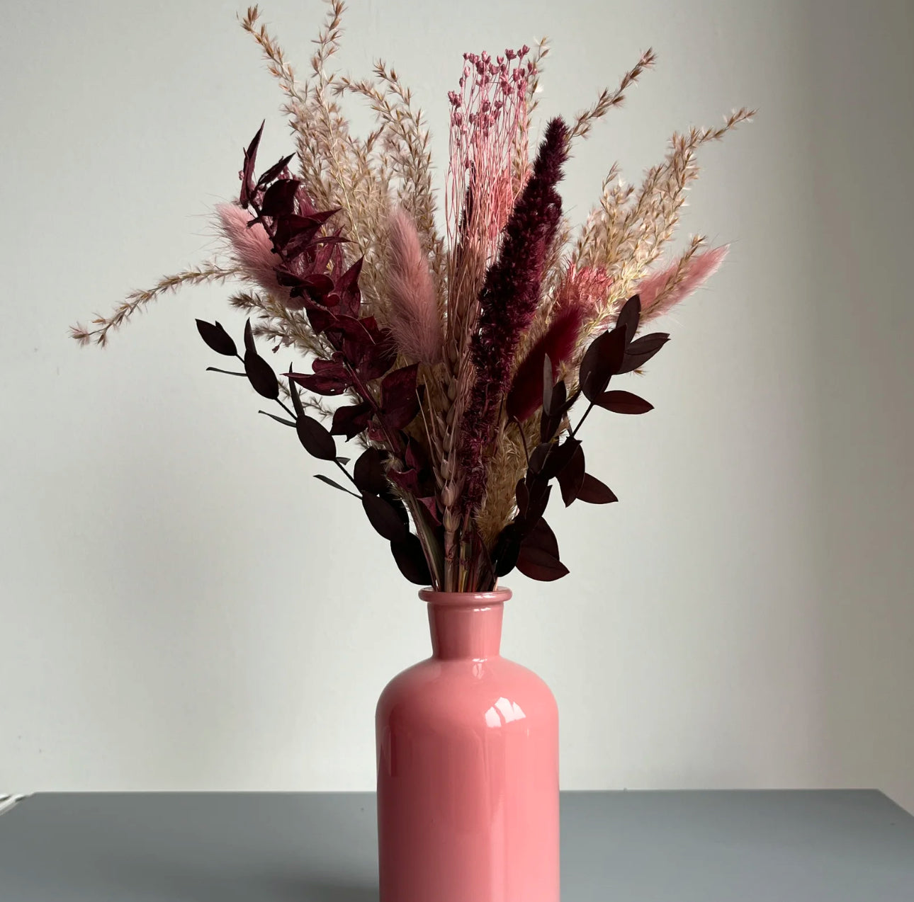 Pink bottle vase displayed on a table with dried flowers