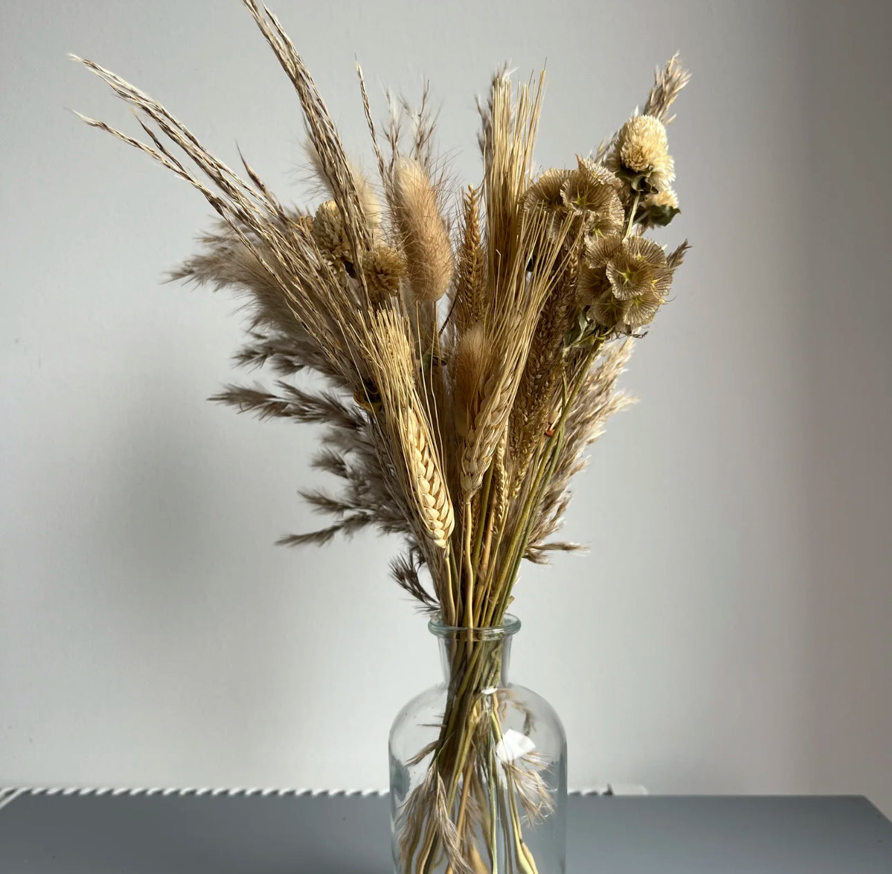 Clear bottle vase displayed on a table with dried flowers