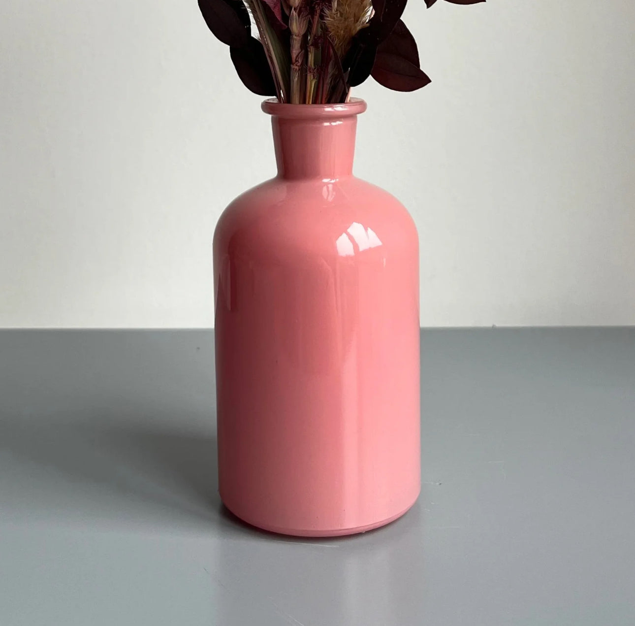 Pink bottle vase displayed on a table with dried flowers