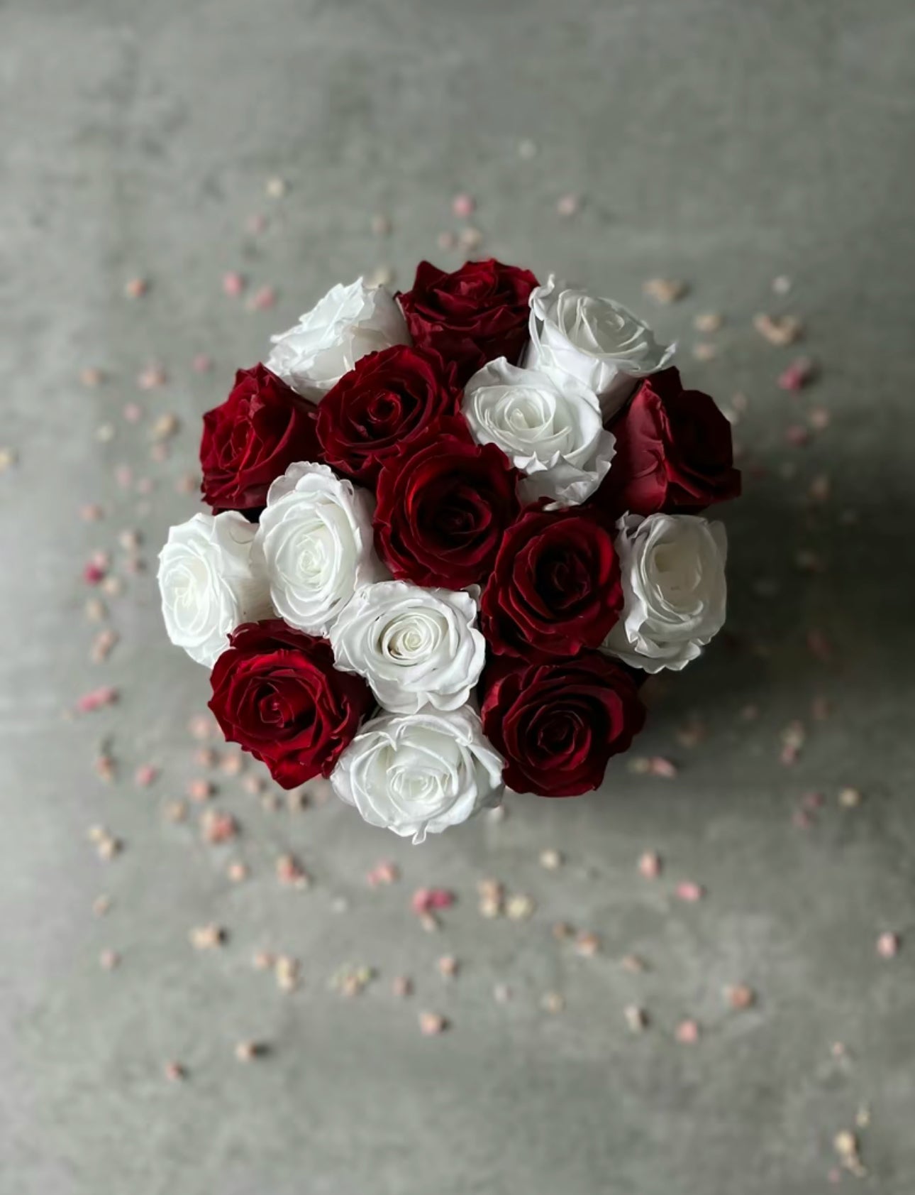 Birds eye view of Preserved dried red and white roses in a velour floristry hat box displayed on a table