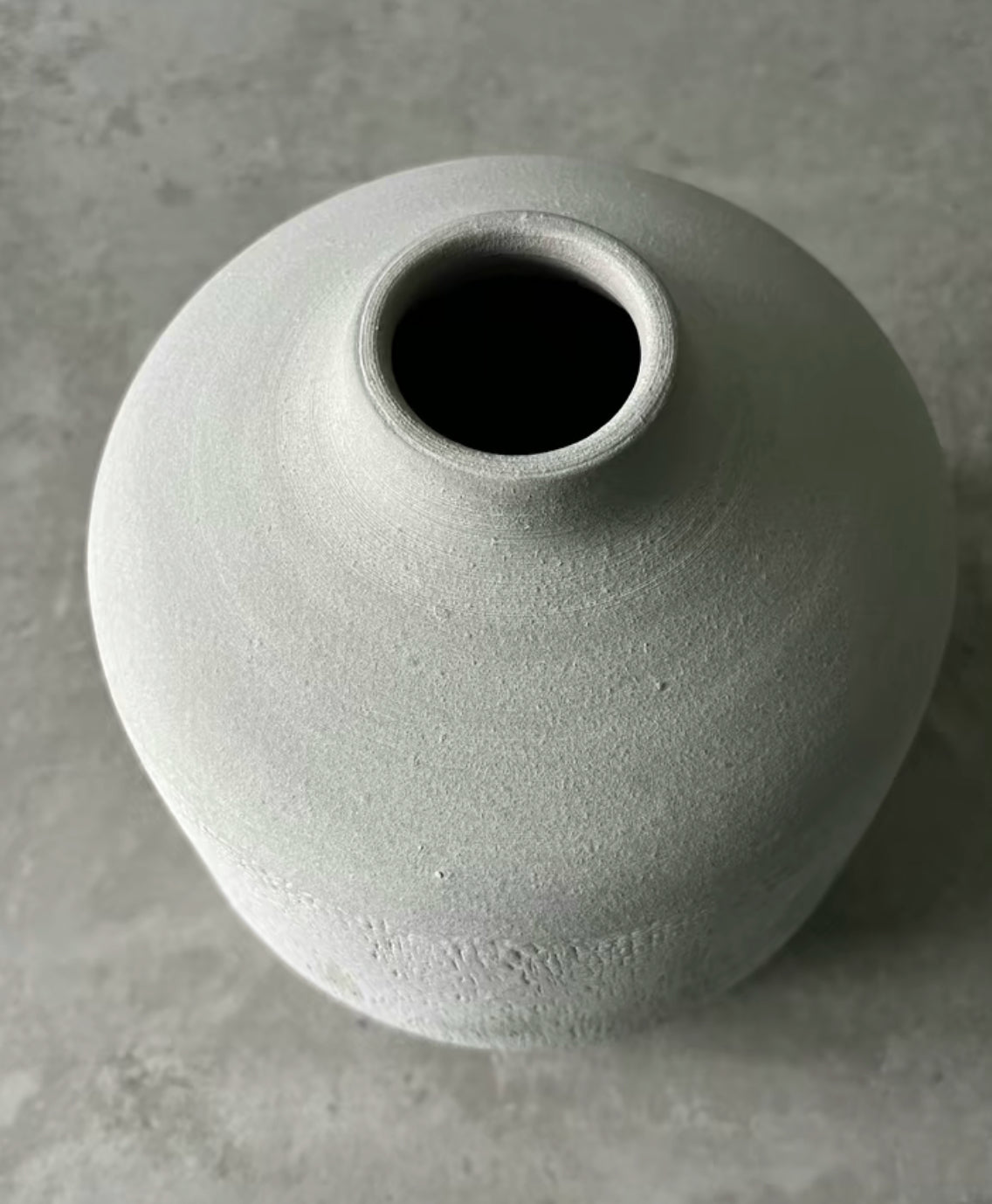 The top of a terracotta stone colour vase in the shade grey being displayed on a table